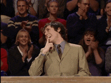 a man in a suit and tie is laughing in front of a crowd of people