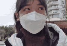 a woman wearing a white face mask looks to the side