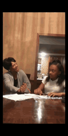 a woman and a girl are sitting at a table with the name norman freeman written on the bottom