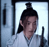 a young man with long hair and a bun is holding a stick .