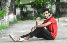 a young man in a red shirt sits on the ground with his feet crossed