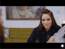 a woman sitting in front of a green couch with a painting on the wall behind her