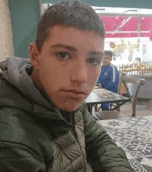 a young boy in a green jacket is sitting at a table in a restaurant .