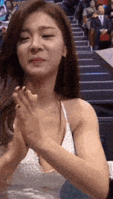 a woman in a white dress is clapping her hands while sitting in a stadium .