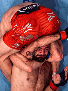 a man wearing red shorts with the word venum on them is wrestling another man