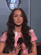 a woman in a pink dress has blood on her face and is holding a microphone