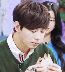 a man in a green sweater is eating a sandwich with kb52 on the bottom