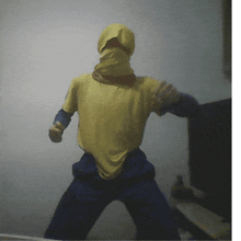 a person wearing a yellow shirt and blue pants has their face covered