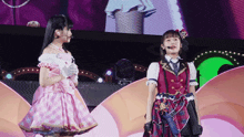 a girl in a pink dress stands next to another girl in a plaid dress