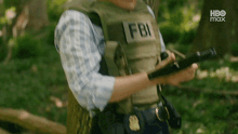 a man in a fbi vest is holding a gun in his hands .