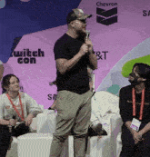 a man is speaking into a microphone in front of a twitch con sign