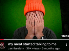 a man wearing an orange hat is covering his face with his hands