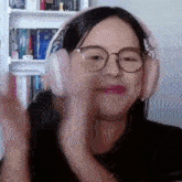 a woman wearing headphones and glasses is smiling and waving her hands .
