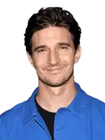a man in a blue shirt and black shirt smiles for the camera