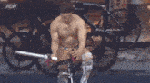 a shirtless wrestler is riding a bike with a aew logo in the background