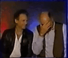 two men are sitting next to each other and one of them is covering his mouth with his hand .