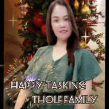 a woman is standing in front of a christmas tree with the words happy tasking tholf family below her