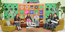 a group of girls are sitting on a couch in front of a spotify sign