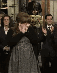 a woman in a grey dress stands in front of a group of people clapping