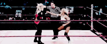 two women are wrestling in a wrestling ring with a referee in the background .