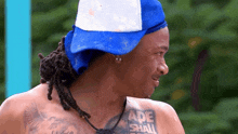 a shirtless man wearing a blue and white hat has a tattoo on his arm that says made shall