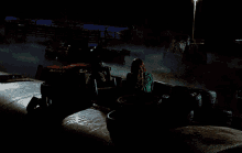 a woman in a green jacket sits in front of a pile of tires in a dark room