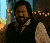 a man with a beard is wearing a black vest and tie .