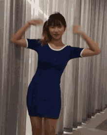 a woman in a blue dress is standing in front of a curtain