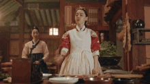 a woman in a red and white apron stands in a kitchen