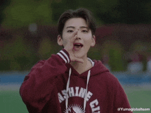 a young man wearing a maroon hoodie is standing on a track and waving his hand .
