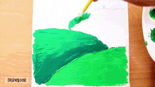 a person is painting a green landscape on a canvas with drawbook in the corner