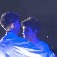 two men are hugging each other in a dark room with blue lights behind them