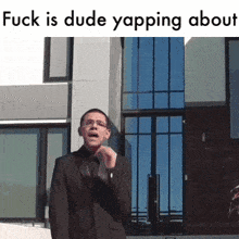 a man in a suit stands in front of a building with the words " fuck is dude yapping about "