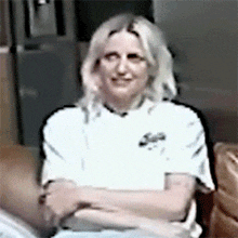 a woman wearing a white shirt with the letter s on it is sitting on a couch with her arms crossed