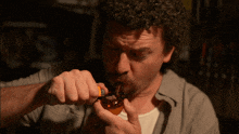 a man with curly hair is drinking from a glass bottle