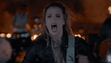 a woman in a leather jacket is screaming with a guitar strap that says ' a ' on it