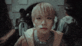 a young man with blonde hair and a star necklace looks at the camera