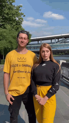 a man wearing a yellow shirt that says dolce & gabbana stands next to a woman