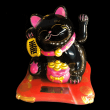 a statue of a black cat with a pink collar and a yellow bag that says " hhh "