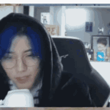 a woman with blue hair and glasses is sitting in a chair .