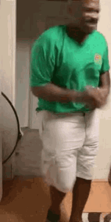 a man in a green t-shirt and white shorts is dancing in a room .