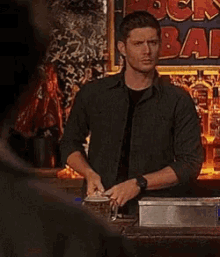 a man is standing in front of a bar with bottles of alcohol on it .