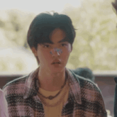 a young man wearing a plaid shirt and a necklace is sitting at a table with a butterfly on his nose .