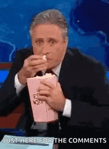 a man in a suit is eating popcorn while sitting on a stage .