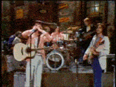 a man singing into a microphone while playing a guitar in front of a drum set