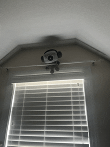 a stuffed monkey hanging from the ceiling above a window with blinds