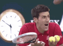 a man in a red shirt is holding a tennis racquet and three tennis balls .