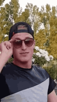 a man wearing sunglasses and a baseball cap is adjusting his sunglasses .