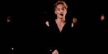 a man in a black shirt is standing in the dark with a microphone .