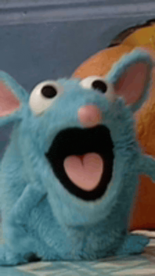 a blue stuffed animal with a pink heart in its mouth is sitting on a bed .